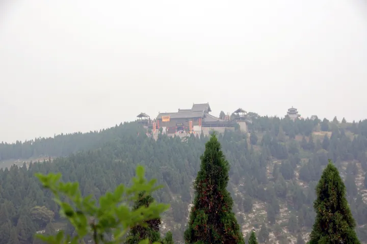 Temple buildings on a forested hilltop seen from a distance