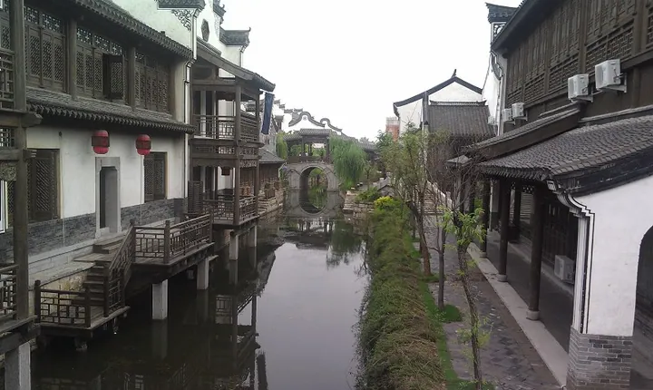 A canal running between rows of traditional Chinese buildings, with lanterns and an arched stone bridge