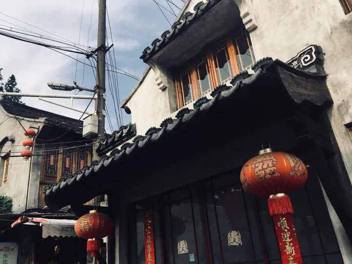 Upward view of tiled eaves and hanging red lanterns on an old building in Fengjing Ancient Town