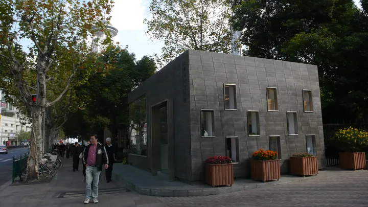 The cube-shaped stone-and-glass building of MOCA Shanghai, with pedestrians on the tree-lined street outside