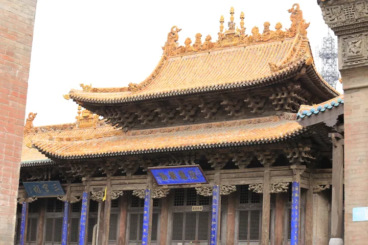 Ornate glazed yellow-and-green tiled roof and carved wooden façade of a temple hall