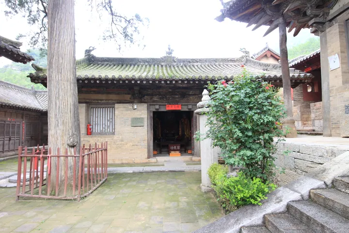 A traditional tiled-roof side hall with a large tree in the courtyard of Longmen Temple