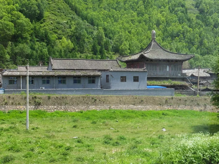 Temple buildings with a golden-roofed hall set against green mountain slopes