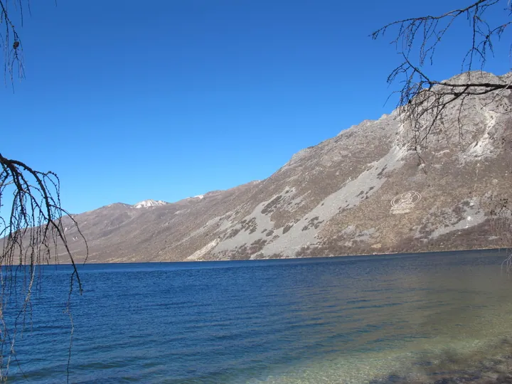 Deep blue alpine lake bordered by bare mountains under a clear sky.