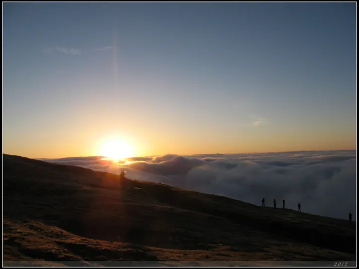 Silhouetted hikers watching sunrise over a cloud sea from a mountain ridge