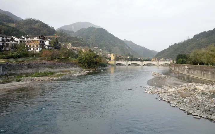 A traditional riverside town with a stone bridge and mountain backdrop