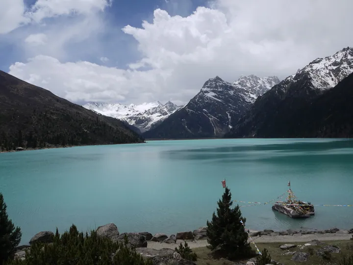 A turquoise glacial lake with prayer flags, backed by snow-capped mountains