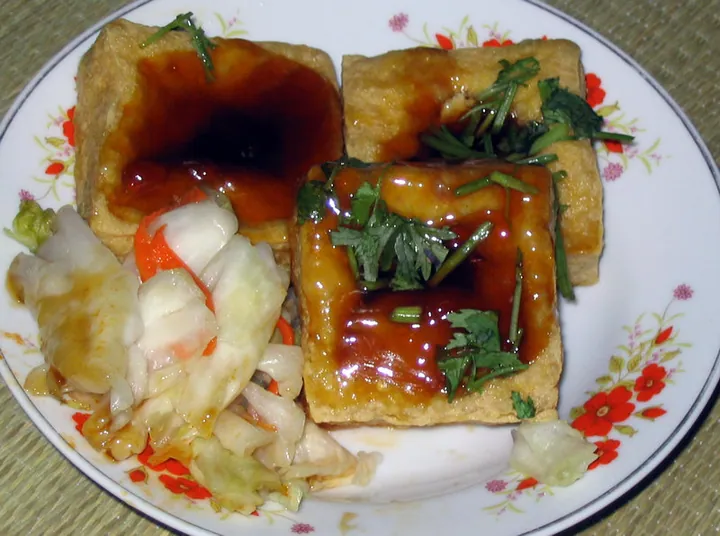 Plate of fried stinky tofu cubes with chili sauce and pickled cabbage