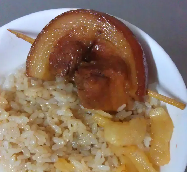 A close-up of a slice of braised pork belly over rice.