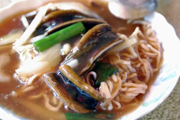 A bowl of noodles topped with eel pieces in thick sauce.