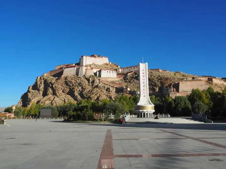Fortress on a rocky hill with a memorial obelisk in the foreground plaza