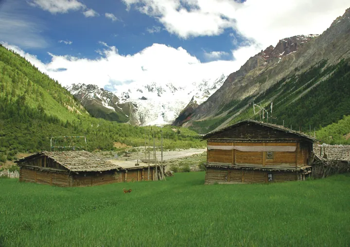 White glacier tongue above a green valley with traditional wooden houses