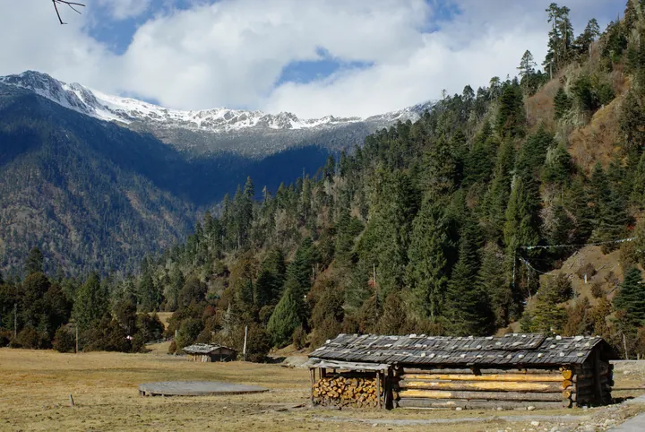 Valley landscape with snow-capped mountains, forest and traditional wooden cabins