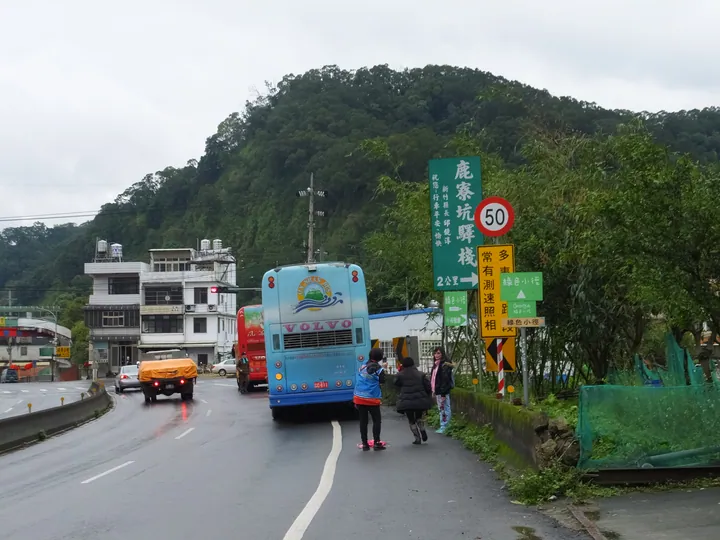 A small-town street with a bus and destination sign for Luliaokeng, hills in the background