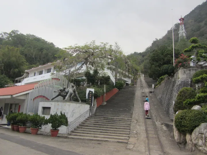 A stone staircase and old rail track leading up a wooded hillside past a memorial statue