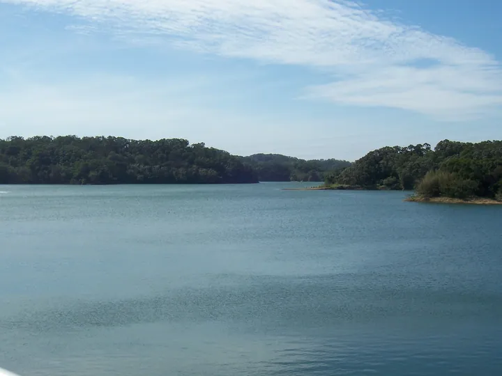 A calm reservoir surrounded by forested hills under a blue sky