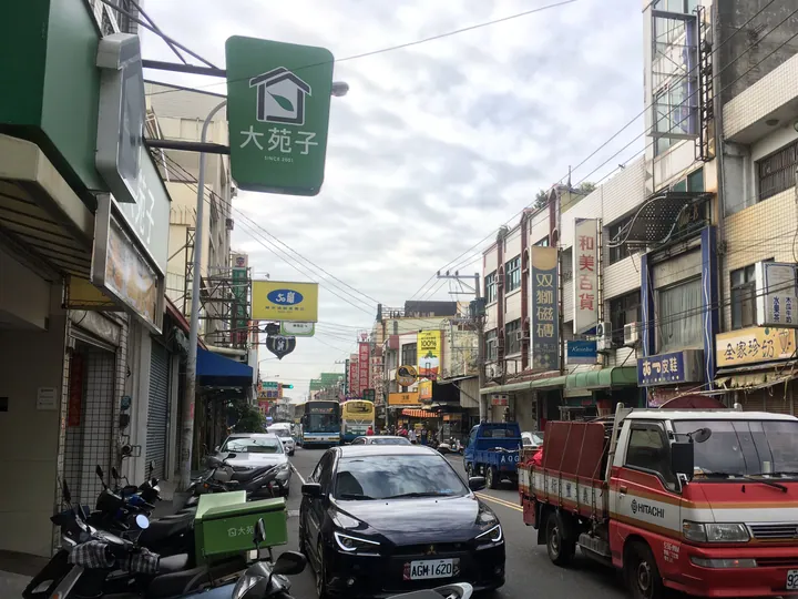 A busy commercial street with shop signs, scooters and vehicles