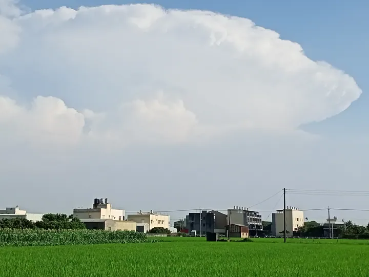 Rice paddies and village buildings under a large cloud formation in Puyan Township