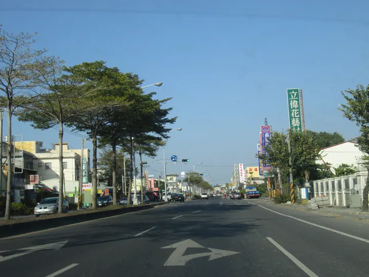 A small-town street lined with shops and trees under a blue sky