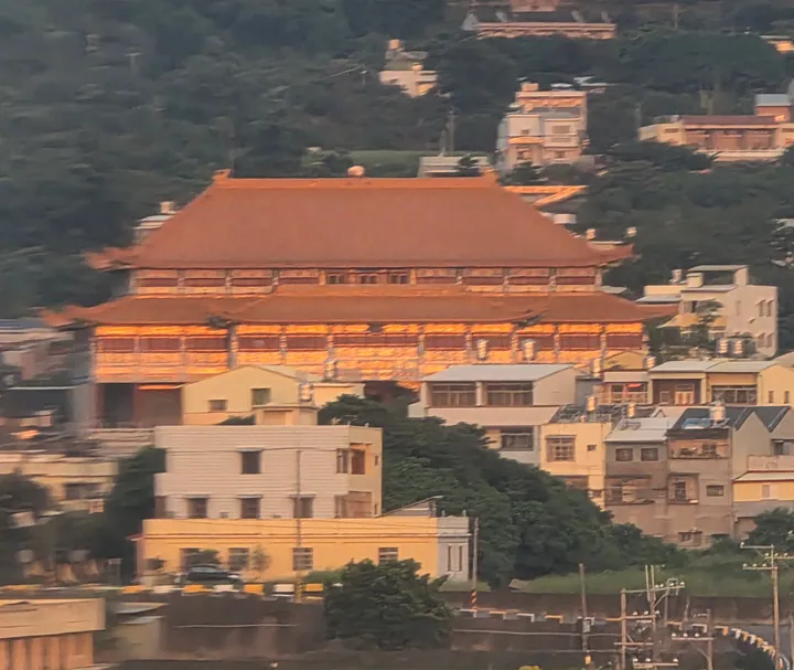 A golden-roofed temple building rising above houses on a wooded hillside