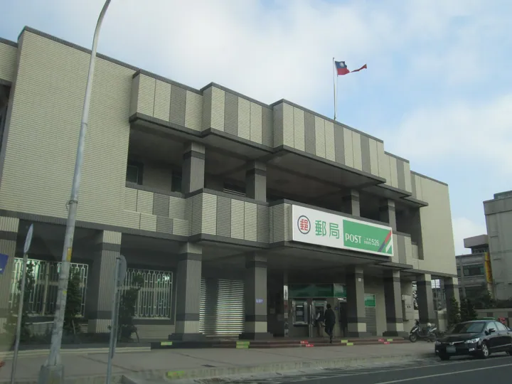 A modern post office building with the national flag flying above the entrance