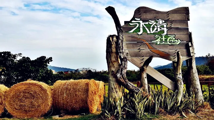 Wooden welcome sign and rolled hay bales with hills behind, Manzhou Township