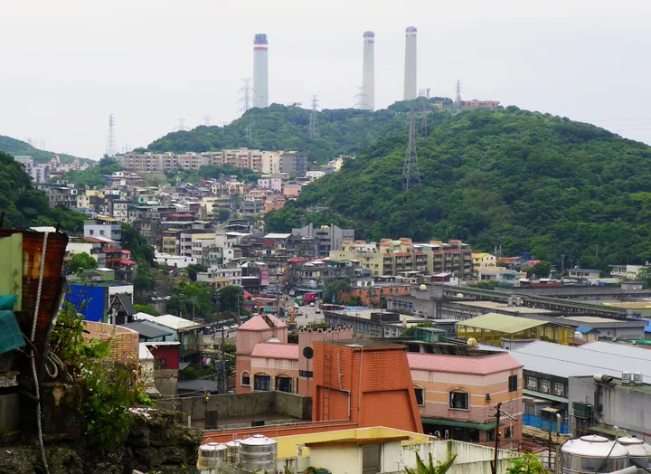 Dense hillside housing in Zhongshan District with tall chimneys on the ridge behind