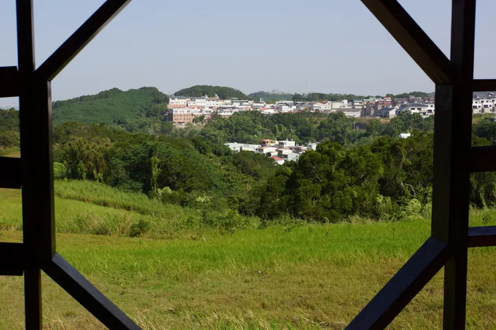 Green grassland and hillside houses seen through an ornate window frame in Xiangshan District