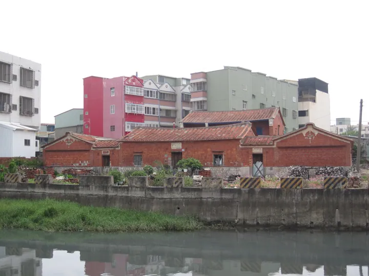 Old red-brick tiled-roof building reflected in a canal with modern apartments behind