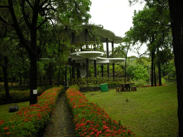 Multi-tiered park pavilion surrounded by red flowering shrubs in Niaosong District