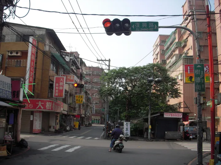 Urban street intersection with a traffic light, road-name sign and shopfronts in Shulin District, New Taipei
