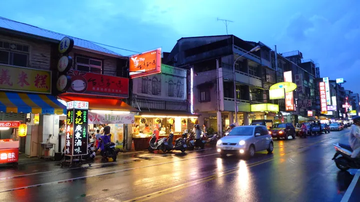 Evening street scene with illuminated shop signs and passing traffic at Zhongxiao Night Market, South District, Taichung
