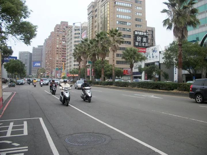 A palm-lined city street with scooters and high-rise buildings in Nantun District