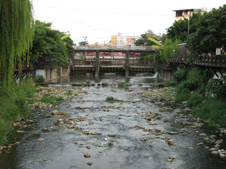 Willow-lined river with a footbridge in Daya District