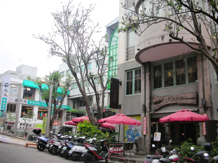Street lined with cafes, red patio umbrellas and parked scooters on an art street in Longjing District, Taichung