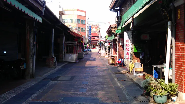 A narrow old street with shop awnings and a temple roof visible in the distance, in Dali District
