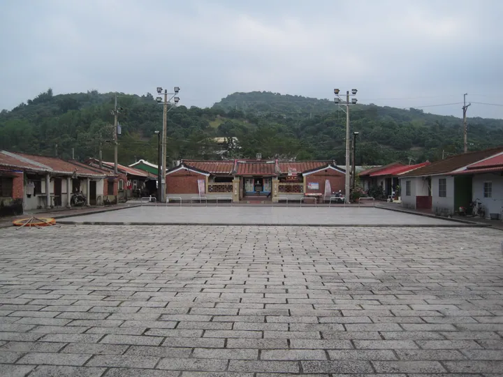 A traditional courtyard village with red-tiled roofs and hills behind, in Nansi District