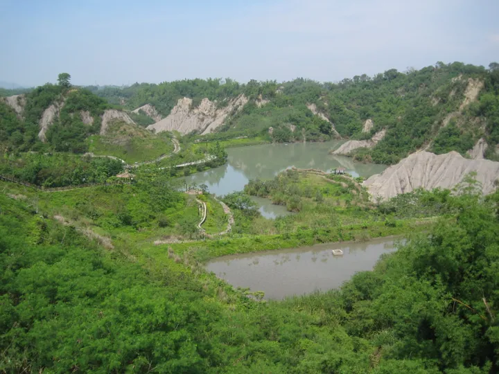 Scenic lake surrounded by eroded mudstone badlands and greenery in Longci District, Tainan