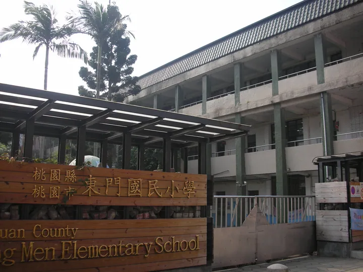 School building entrance with palm trees and a sign reading Dong Men Elementary School, Taoyuan County