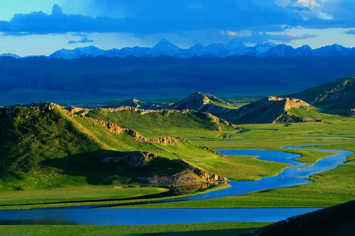 A winding river through the green Bayanbulak grassland at golden hour