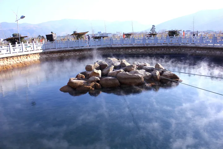 Round stone-rimmed hot-spring pool with rising steam and mountains in the background