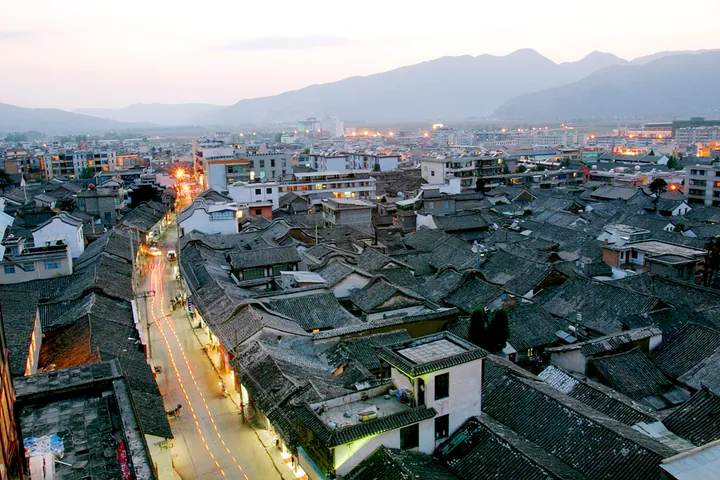 Twilight elevated view of an old town's grey tiled roofs with mountains behind