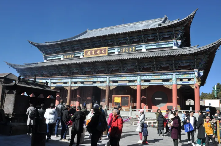 Ornate Buddhist temple hall with visitors in front under a blue sky