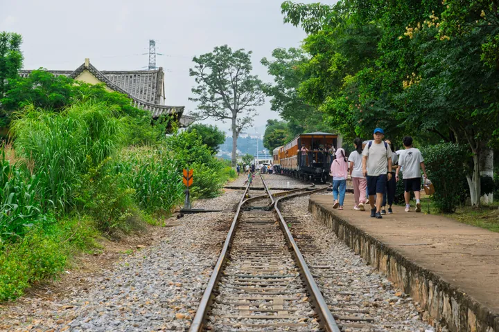 Narrow-gauge railway track and heritage train carriage beside a platform with walking tourists