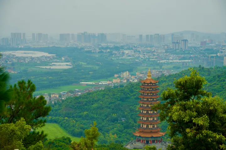 A tall multi-tiered pagoda on a green hillside overlooking the hazy skyline of Mile