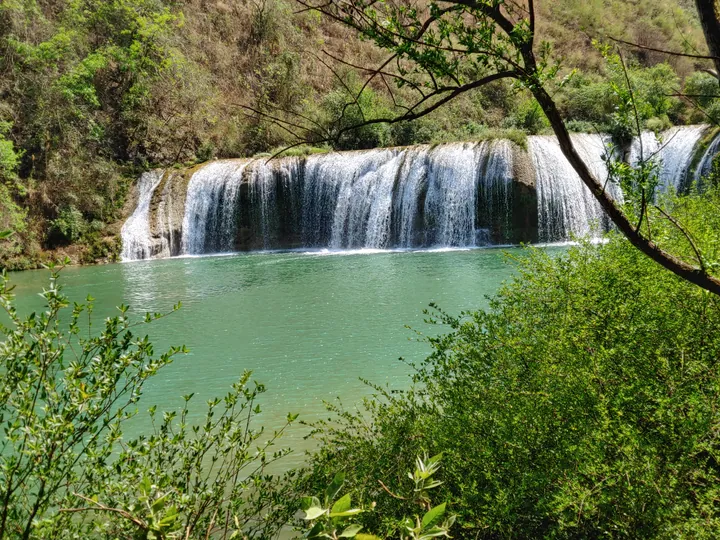 Wide waterfall cascading into a turquoise pool surrounded by greenery