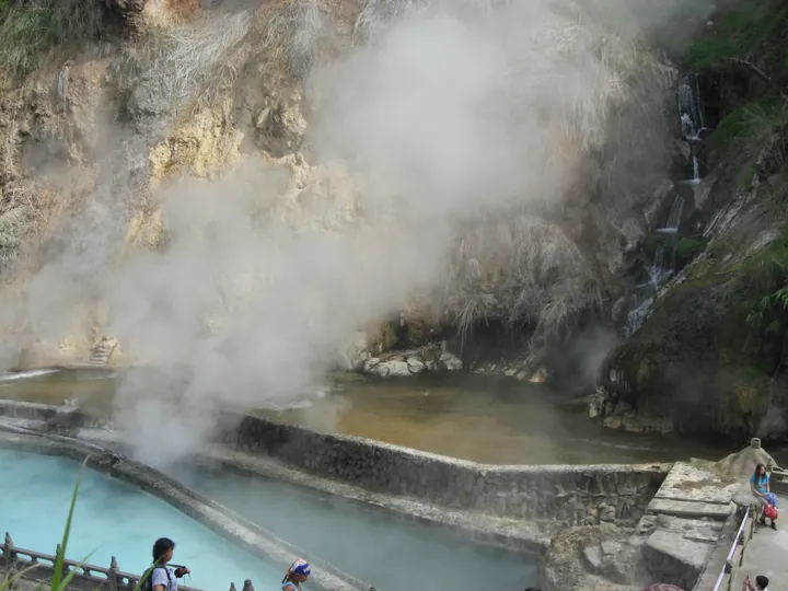 Terraced turquoise hot-spring pools with rising steam against a rocky hillside