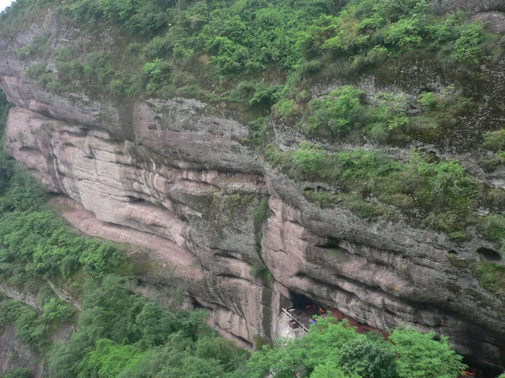 Reddish sandstone cliff with a small temple built into an alcove