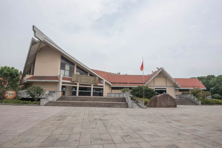 A modern museum building with an angular sail-shaped roof and wide entrance plaza