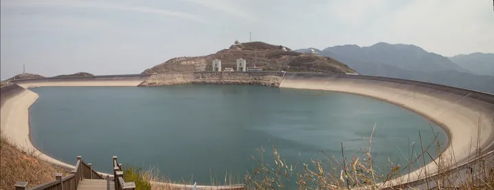Panoramic view of a circular mountaintop reservoir ringed by a paved dam wall